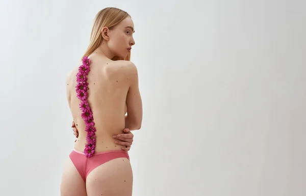 Vue arrière de la jeune femme caucasienne à moitié nue avec un corps mince en forme portant des culottes posant avec des fleurs roses le long de son dos — Photo