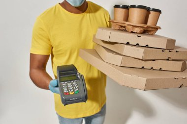 Koruyucu eldivenlerle pizza dağıtan adam kutuları taşırken ve kredi kartıyla ödeme yapmak için terminale uzanırken.