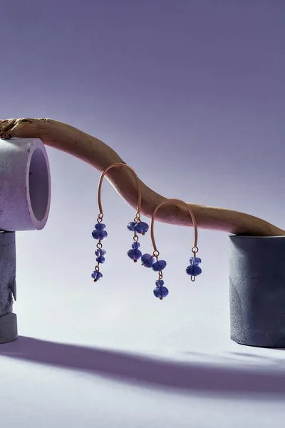 Foto creativa de pendientes asimétricos hechos a mano con cuentas de color púrpura en palo de madera aislado sobre fondo de degradado púrpura claro —  Fotos de Stock