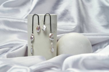 Şirin doğal inci küpeler gri ipek arka planda asılı.