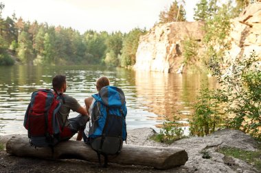 Göl kenarında oturan genç beyaz çiftin arka manzarası.