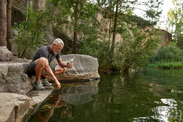 Garrafa de enchimento turístico masculino com água do lago — Fotografia de Stock