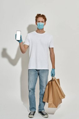 Bir elinde akıllı telefon, diğer elinde kağıt torba olan bir kuryenin dikey görüntüsü.