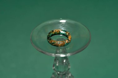 İçinde altın folyo bulunan epoksi reçineden yapılmış, yeşil arka planda izole edilmiş şarap kadehinin yaratıcı el yapımı yüzüğü.