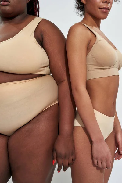 Przycięte ujęcie dwóch afrykańskich kobiet w beżowej bieliźnie o różnej wadze stojących blisko siebie na szarym tle — Zdjęcie stockowe
