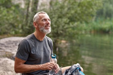 Gülümseyen orta yaşlı beyaz adam kütüğün üzerinde dinleniyor.