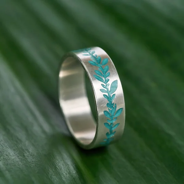 Μακρο βολάν από ασημί μεταλλικό δαχτυλίδι με τυρκουάζ floral μοτίβο σμάλτο απομονωμένο πάνω σε πράσινο φόντο φύλλων — Φωτογραφία Αρχείου