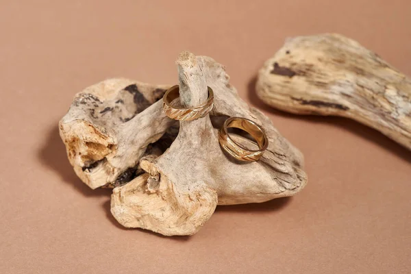 Δύο κομψά χρυσά δαχτυλίδια με εγκοπές τοποθετημένες σε ξύλινο στοιχείο πάνω από μπεζ φόντο — Φωτογραφία Αρχείου