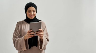 Tablet arayan tesettürlü, tatlı, genç bir Arap kadın.