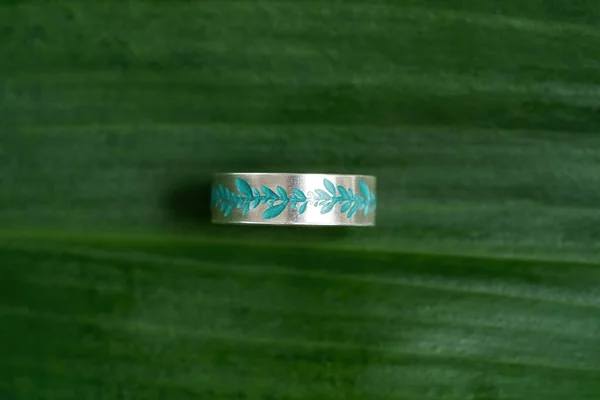 Κάτοψη από ασημί μεταλλικό δαχτυλίδι με τυρκουάζ floral μοτίβο σμάλτο απομονωμένο πάνω σε πράσινο φόντο φύλλων — Φωτογραφία Αρχείου