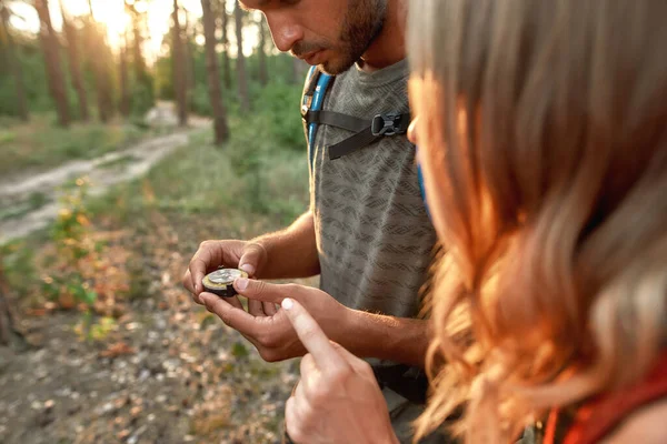 Young couple of tourists holding a compass and looking for direction navigation while walking together in the forest — Stock Photo, Image