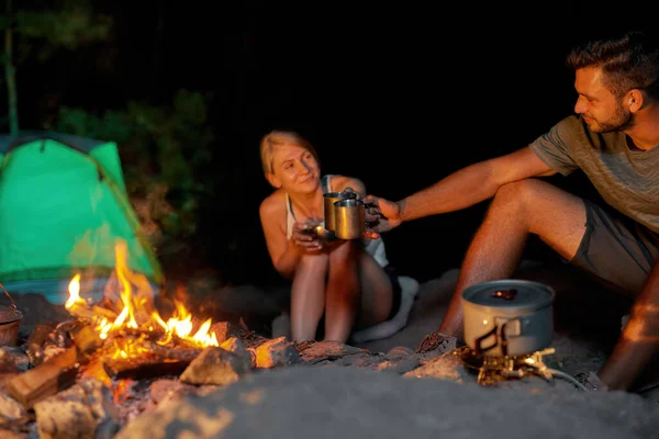 Néhány fiatal turista kávét vagy teát iszik étkezés közben, együtt pihennek a tábortűz közelében a vadonban. — Stock Fotó