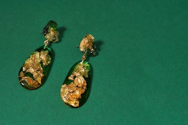 Draufsicht auf Ohrhänger aus Epoxidharz mit goldener Folie innen isoliert über grünem Hintergrund — Stockfoto
