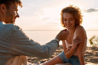 Genç beyaz adam gülen kadını besliyor.