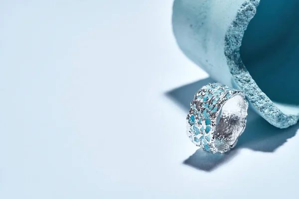 Macro shot de um anel de metal prateado com esmalte azul dispostos com elemento de concreto azul industrial isolado sobre fundo claro — Fotografia de Stock