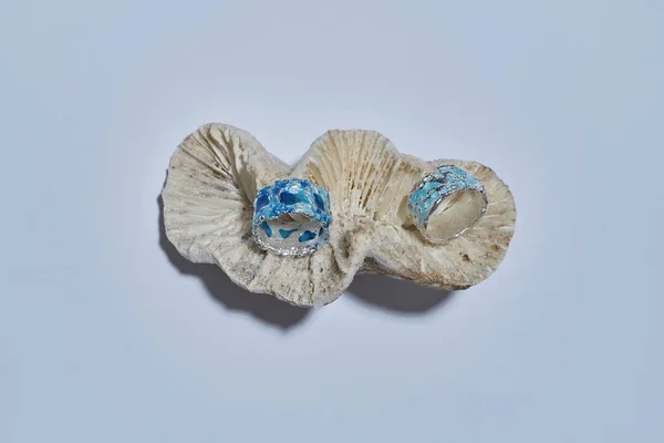 Zwei handgefertigte Ringe aus silbernem Metall mit blauem Emaille verziert mit Muscheln isoliert über hellem Hintergrund — Stockfoto
