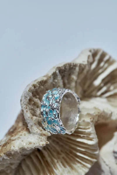 Closeup της μόδας ασημένιο μεταλλικό δαχτυλίδι διακοσμημένα με μπλε σμάλτο που διοργανώνονται με κοχύλια απομονώνονται πάνω από το φως φόντο — Φωτογραφία Αρχείου