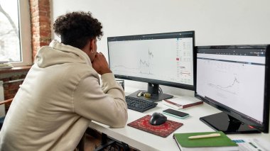 Merkez büroda otururken bilgisayar ekranına bakan ve istatistikleri analiz eden genç adamın dikiz görüntüsü