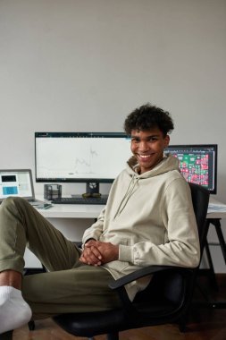 Mutlu genç adam, evde bilgisayar ve dizüstü bilgisayar kullanarak modern oturma odasında oturan melez tüccarlar.