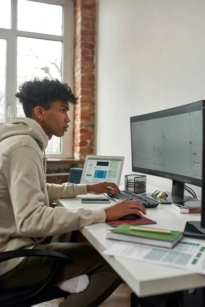 Seitenansicht eines jungen Mannes, der an der Börse handelt und Computer benutzt, während er zu Hause im Wohnzimmer im Büro sitzt — Stockfoto