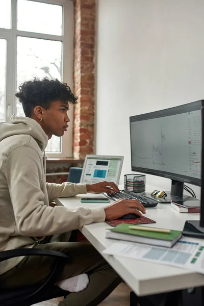 Vista lateral de chico joven que negocia en la bolsa de valores, el uso de la computadora mientras está sentado en la oficina de la sala de estar en casa —  Fotos de Stock