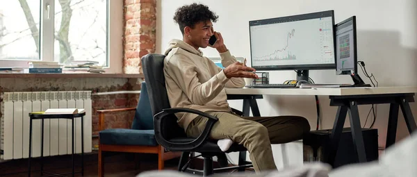 Erfolgreicher junger männlicher Händler telefoniert, diskutiert am Schreibtisch im heimischen Wohnzimmer über den Aktienmarkt — Stockfoto