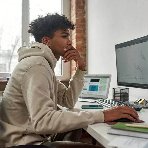 Hombre joven mirando la pantalla de la PC mientras que negocia, haciendo el dinero en línea usando la computadora, sentado en casa en la oficina moderna de la sala de estar — Foto de Stock