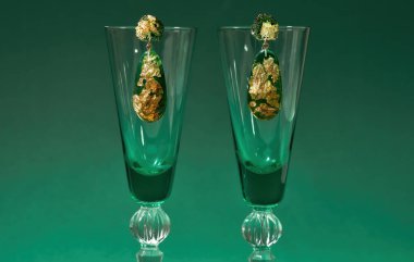 Yeşil arka planda izole edilmiş şarap kadehlerinde altın folyo bulunan epoksi reçineden yapılmış el yapımı küpe.