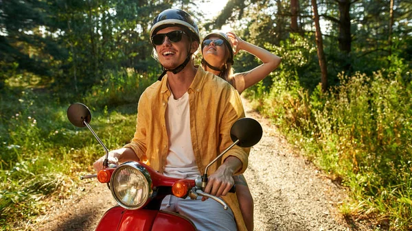 Smiling young caucasian pair riding scooter in wood — Stock Photo, Image