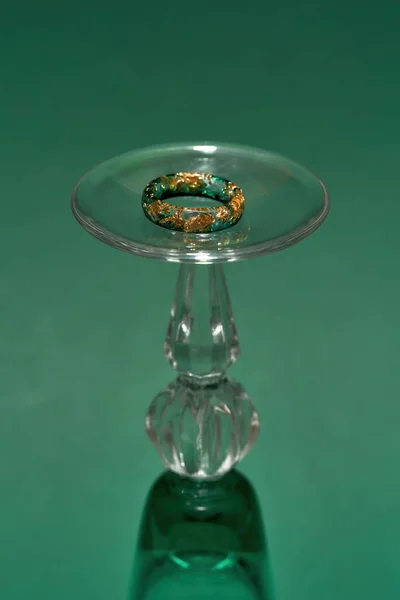 Kreative Aufnahme eines stilvollen, handgefertigten Rings aus Epoxidharz mit goldener Folie innen auf Weinglas isoliert über grünem Hintergrund — Stockfoto