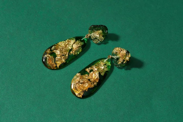 Primer plano de pendientes colgantes hechos de resina epoxi con lámina dorada en el interior aislada sobre fondo verde —  Fotos de Stock