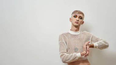 Siyah gece partisi makyajlı genç transseksüel beyaz arka planda yalnız poz verirken kameraya bakıyor.