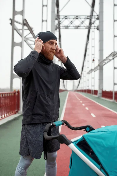 Αθλητικός Νεαρός Πατέρας Που Χρησιμοποιεί Ακουστικά Ενώ Στέκεται Στη Γέφυρα — Φωτογραφία Αρχείου