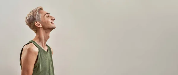 Πορτρέτο του ευτυχούς ανδρογυνή τρανσέξουαλ νεαρός άνδρας ανύψωση του κεφαλιού και χαμογελώντας με τα μάτια κλειστά, ενώ θέτουν απομονωμένη πάνω από το φως φόντο — Φωτογραφία Αρχείου