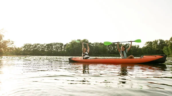 Emocionada joven pareja caucásica levantó los brazos con paletas en ella mientras navegaba en kayak por el río rodeado de naturaleza salvaje —  Fotos de Stock