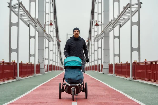 Sportowy młody ojciec biegający z wózkiem w pochmurny dzień w mieście — Zdjęcie stockowe