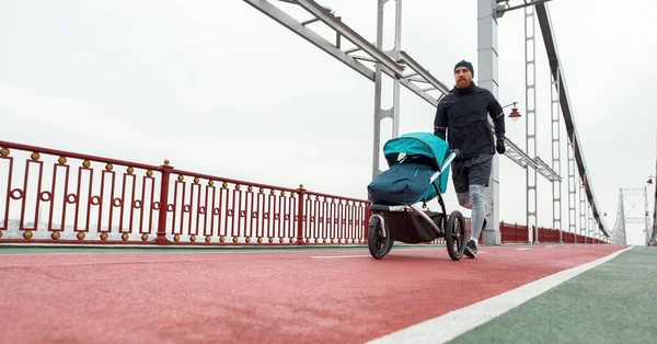 Повнометражний знімок активного молодого батька, що біжить з дитячою коляскою в похмурий день у місті — стокове фото