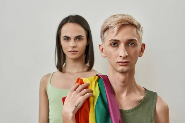 Портрет молодой трансгендерной пары с флагом ЛГБТ, позирующей вместе на светлом фоне — стоковое фото
