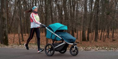 Soğuk bir sonbahar gününde boş bir park boyunca bebek arabasıyla koşan genç bir anne.