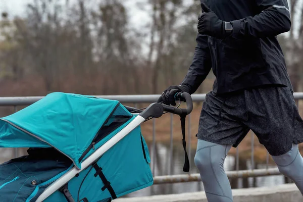 Primer plano de hombre en ropa deportiva trotando con un cochecito en un día frío de otoño — Foto de Stock