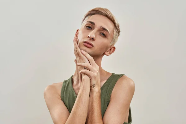 Portret zmysłowego androgynamicznego transseksualisty młodego mężczyzny z makijażem dotykającym twarzy podczas pozowania na jasnym tle — Zdjęcie stockowe