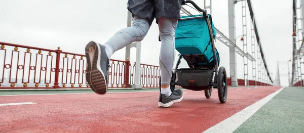 Close up tiro de pernas de pai jovem esportivo motivado correndo com um carrinho em um dia nublado na cidade — Fotografia de Stock