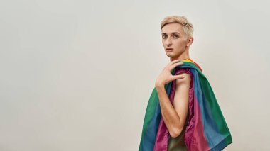 LGBT 'nin renkli gökkuşağı bayrağına sarılı genç transseksüel ışık arkaplanı üzerinde izole poz verirken kameraya bakıyor