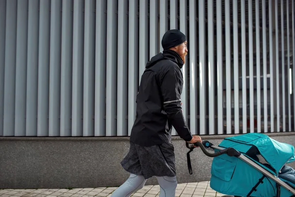 Спортивний молодий тато бігун ходить з коляскою в місті в холодний осінній день — стокове фото