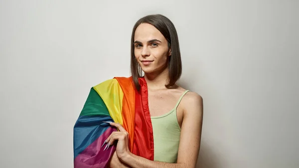 Jovem transgênero com bandeira colorida do arco-íris LGBT olhando para a câmera enquanto posando isolado sobre fundo de luz — Fotografia de Stock