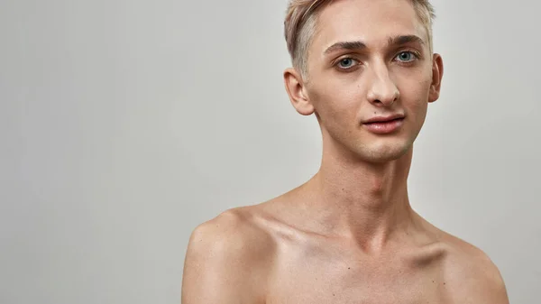 Portret van onverschrokken androgyne transgender jongeman met naakte make-up op zoek naar camera terwijl poseren geïsoleerd over lichte achtergrond — Stockfoto