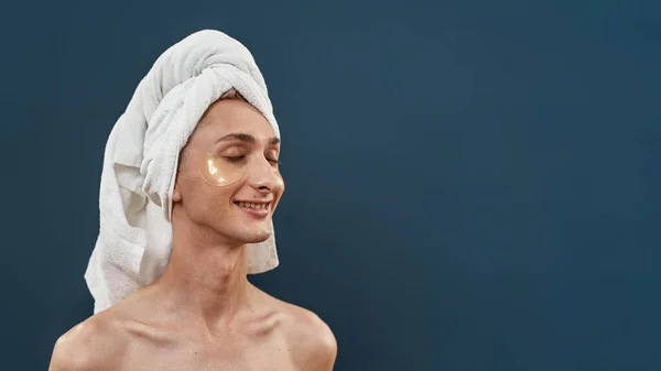 Nackter junger Transgender mit aufgetragenen Augengelflecken und Handtuch auf dem Kopf, der darauf achtet, mit geschlossenen Augen isoliert vor dunklem Hintergrund zu posieren — Stockfoto