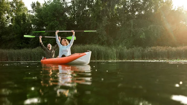 Blij jong stel kijken gelukkig, stak hun handen met peddels in het, terwijl varen samen in de rivier op een zomerse dag — Stockfoto