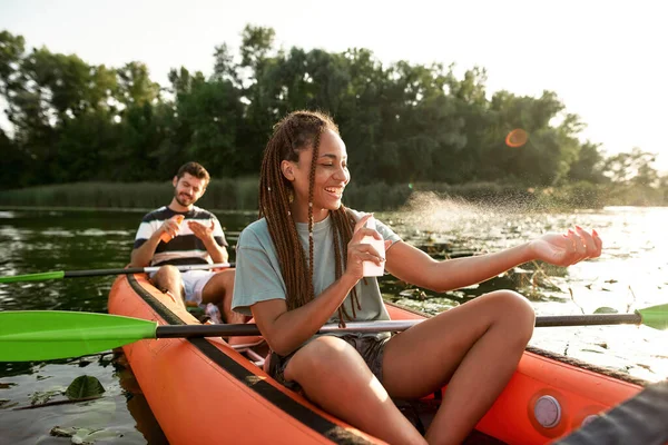Vidám fiatal nő permetez fényvédő miközben kajakozik a folyón a barátjával a szabadban — Stock Fotó