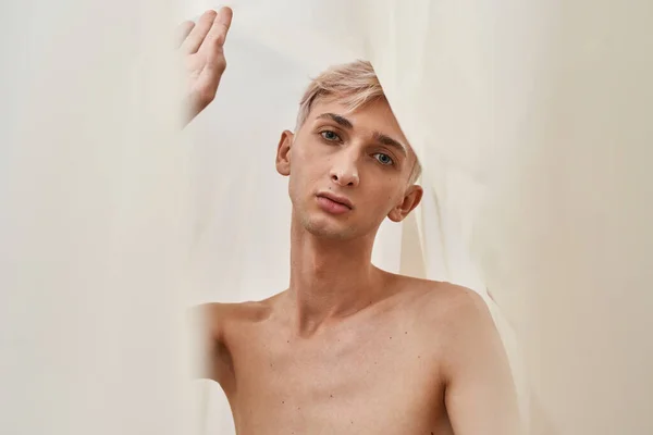 Retrato de joven transgénero suave con maquillaje mirando a la cámara mientras posa aislado sobre fondo de tono pastel claro —  Fotos de Stock